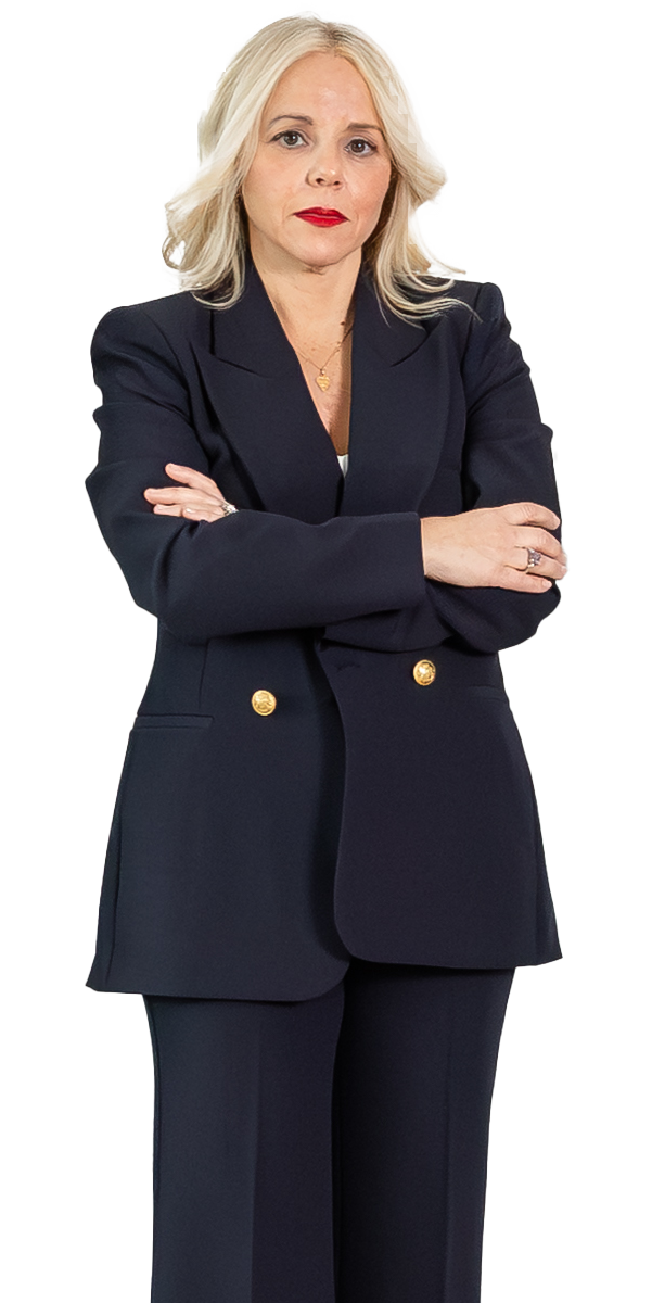 Woman with blonde hair wearing a dark suit stands with arms crossed, facing forward against a plain light background.