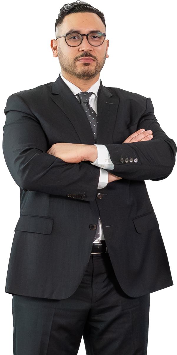 Man in a black suit and polka dot tie standing with arms crossed, facing forward against a plain white background.
