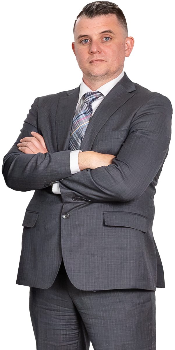 Man in a gray suit and striped tie stands with arms crossed, looking at the camera against a plain white background.