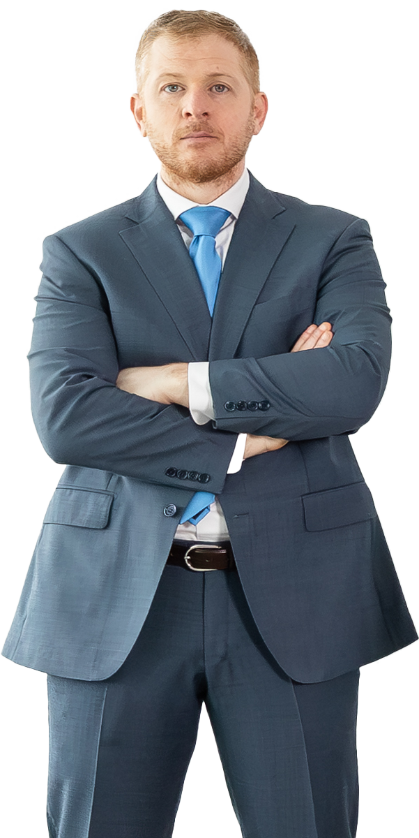 Man in a blue suit and blue tie stands with arms crossed, looking forward against a plain white background.