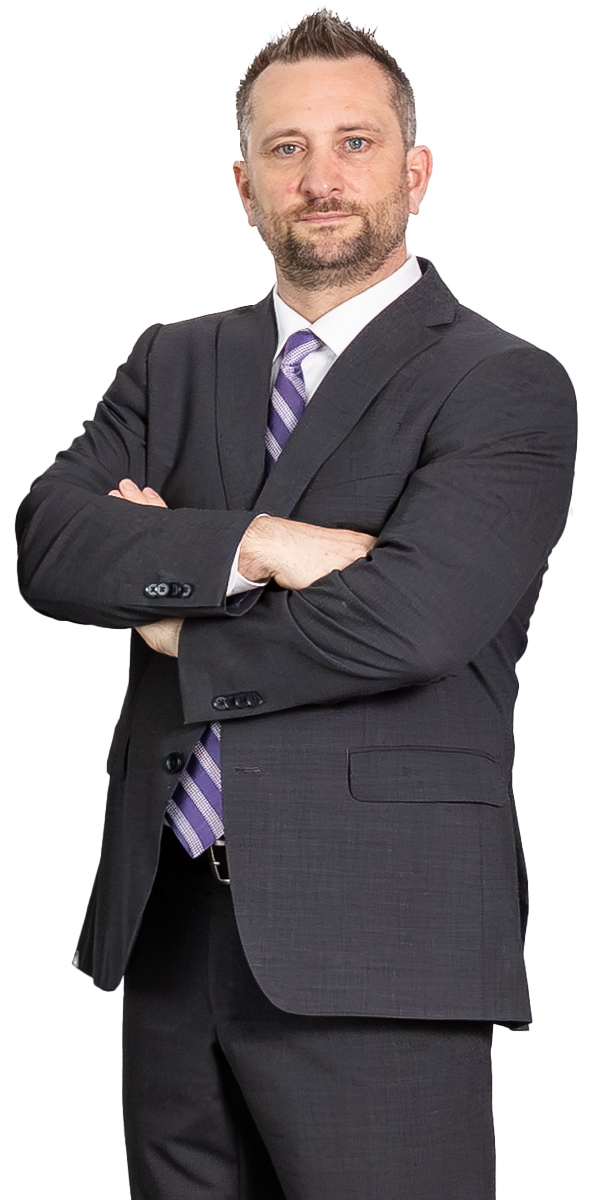 Man in a dark suit with a purple striped tie stands with arms crossed, looking forward, against a plain white background.