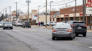 multiple vehicles on busy commercial road with pedestrians and retail storefronts